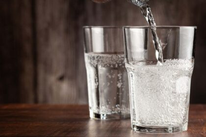 Botella de agua con y sin gas sobre mesa deportiva, junto a toalla y pesas.
