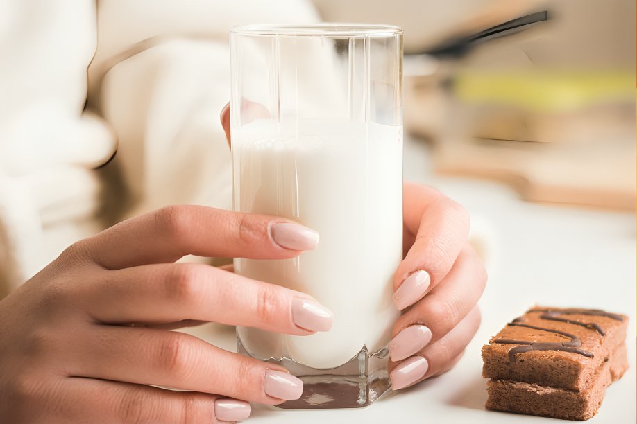 Adulto bebiendo vaso de leche mientras revisa estudios científicos sobre nutrición en mesa de cocina moderna