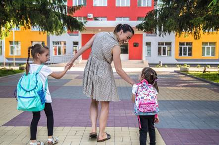 Niño iniciando su primer día de clases acompañado por sus padres en la puerta de la escuela.