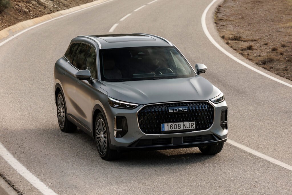 Vista lateral dinámica del SUV híbrido Ebro S900 circulando por un entorno urbano moderno.
