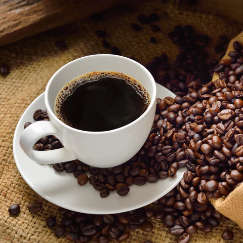 Taza de café humeante con granos de café esparcidos alrededor, simbolizando los beneficios del café para la salud cerebral.