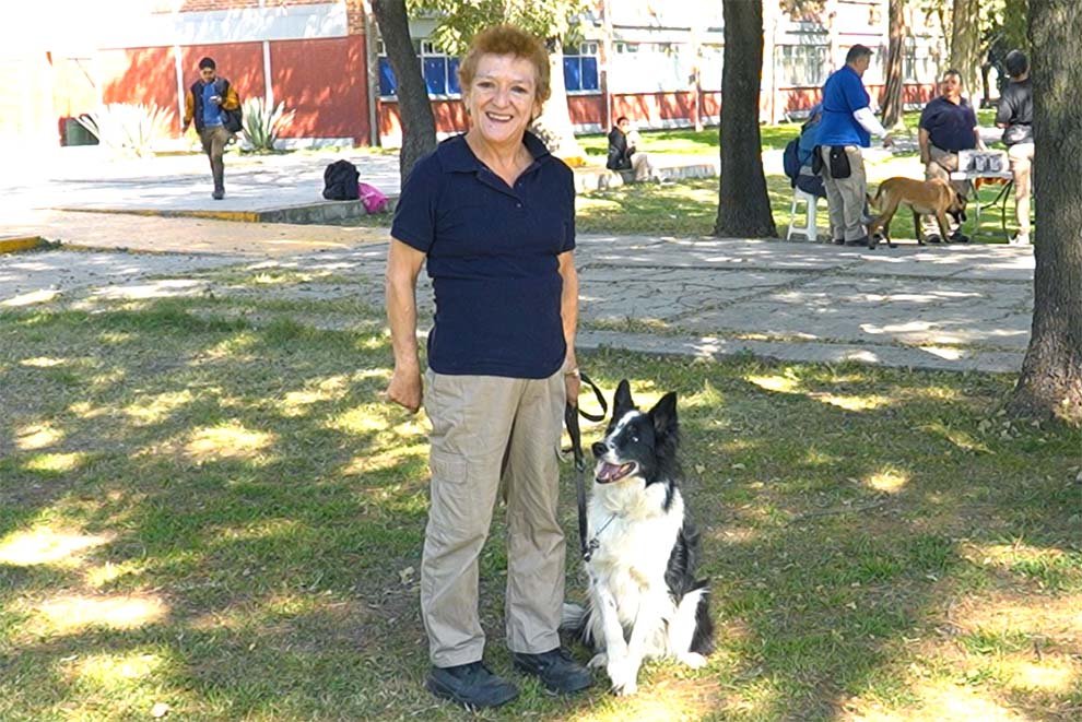 Adulto mayor sonriendo junto a su perro en un parque, disfrutando de un día soleado.