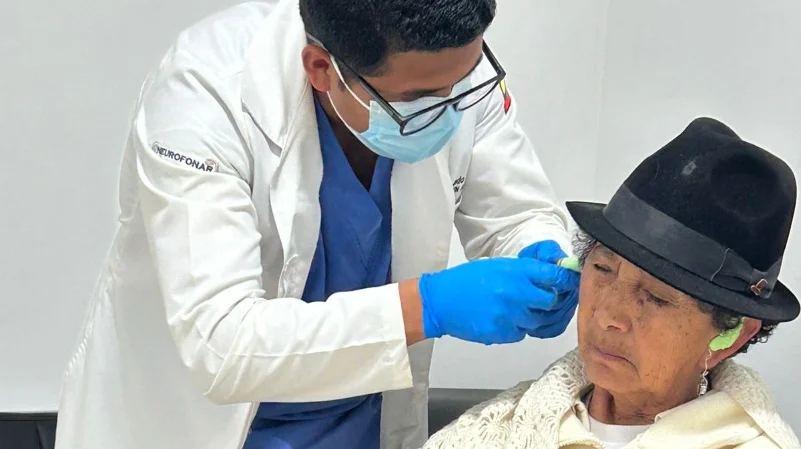 : Persona sonriendo mientras se le realiza un examen de audición con auriculares.