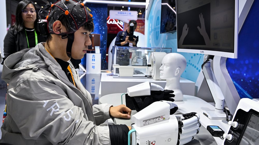 Hombre probando mano robótica controlada por interfaz cerebro-computadora en feria de Shanghái 2025