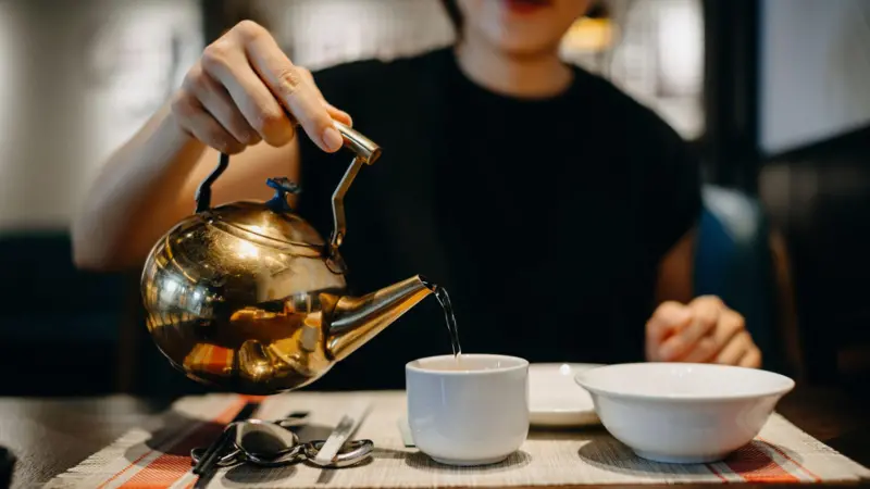 Una persona joven sosteniendo una taza de agua tibia con vapor, con un fondo suave que sugiere un ambiente tranquilo y natural