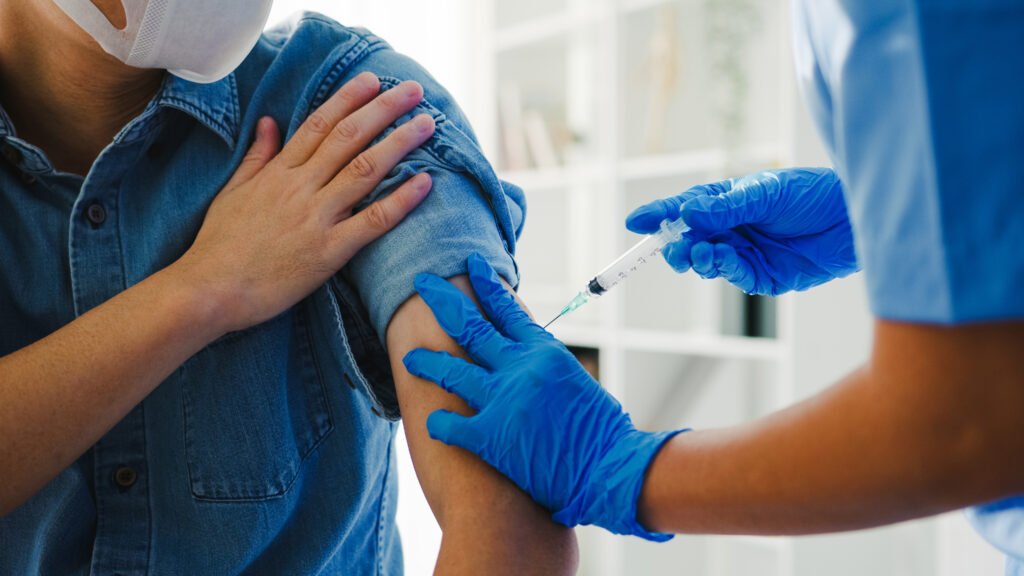 Mujer adulta recibiendo una vacuna en el brazo, con un profesional de la salud administrando la inyección.