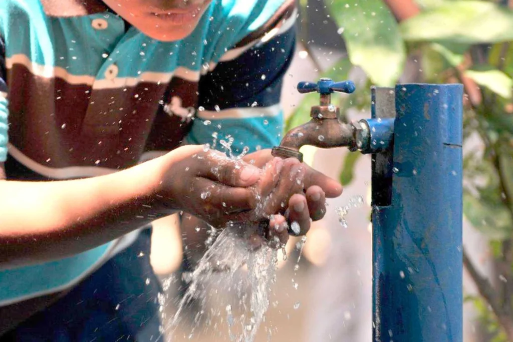 Niño ecuatoriano bebiendo agua limpia de un grifo, simbolizando el acceso a agua potable y saneamiento