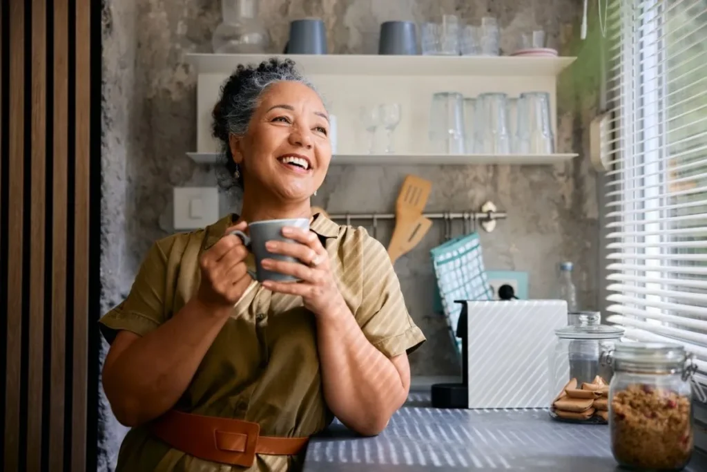 Una persona sonriente disfrutando de una taza de café humeante, con un fondo desenfocado que sugiere actividad cerebral o un entorno saludable.