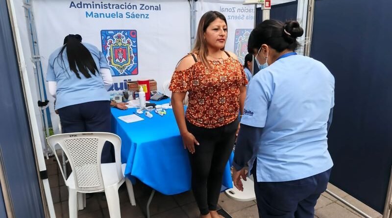 Vista general de una feria de salud municipal, con personal atendiendo a vecinos en una plaza pública de Quito