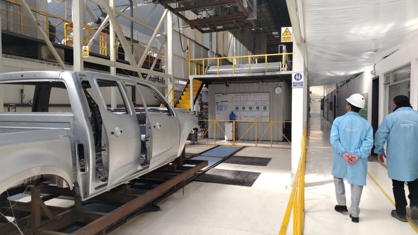 Operarios técnicos ensamblando el chasis de un vehículo moderno dentro de una planta automotriz robotizada en Ecuador.