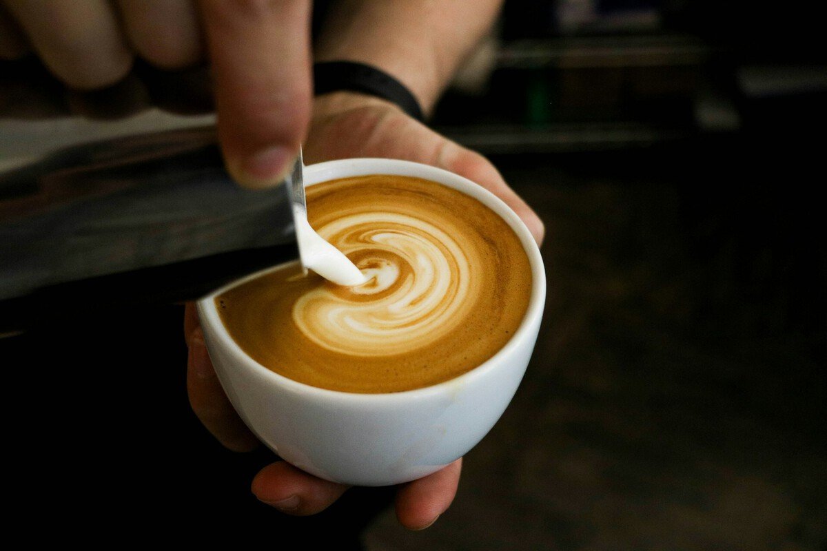 Taza de café humeante sobre una mesa con texto que indica que el problema no es tomar café, sino el consumo excesivo