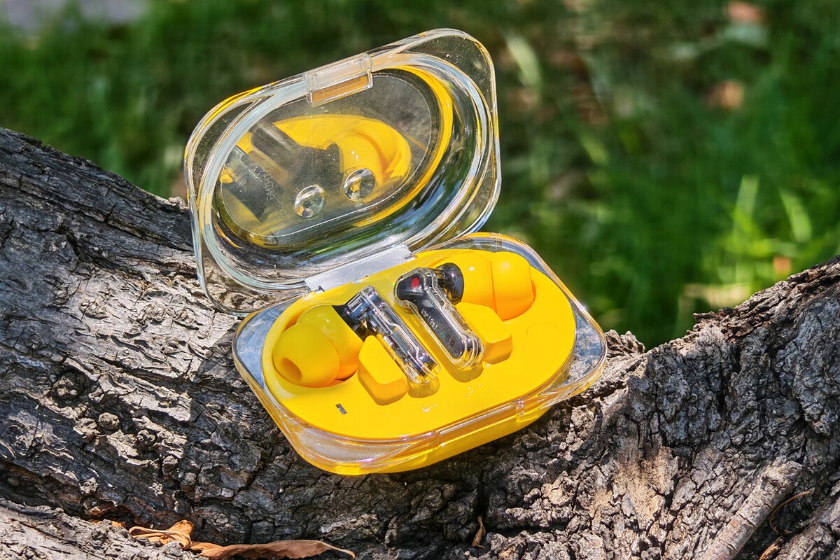 Primer plano de los auriculares inalámbricos transparentes amarillos y su estuche con luces LED de los auriculares Nothing Ear (3a).
