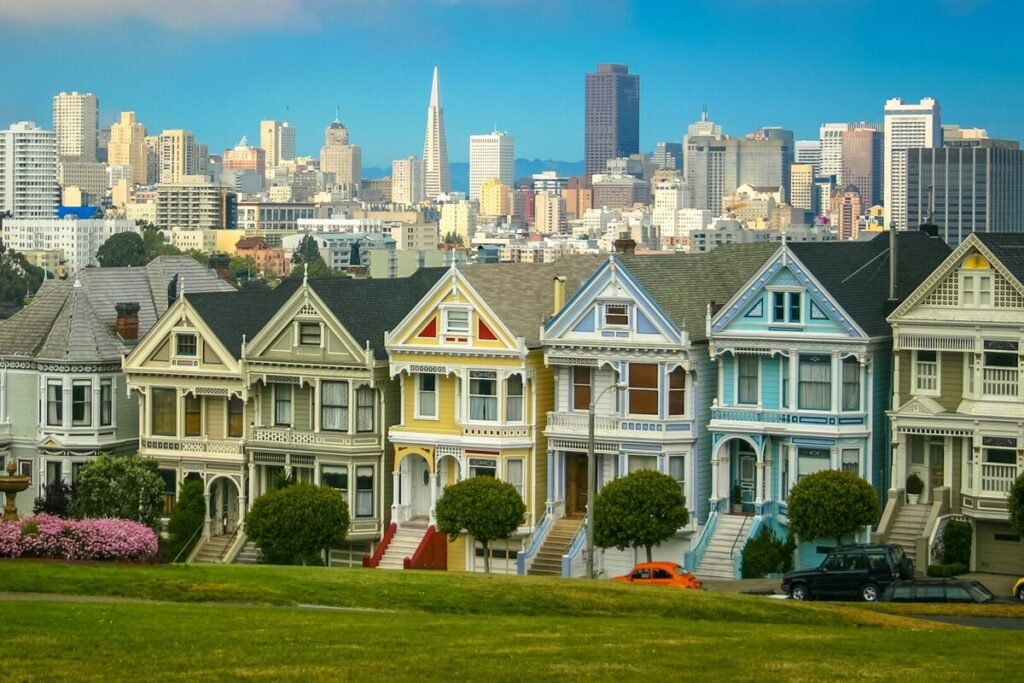 Una hilera de casas residenciales tradicionales de San Francisco con rascacielos corporativos tecnológicos al fondo bajo una densa niebla, ilustrando la crisis para vivir bien en San Francisco.