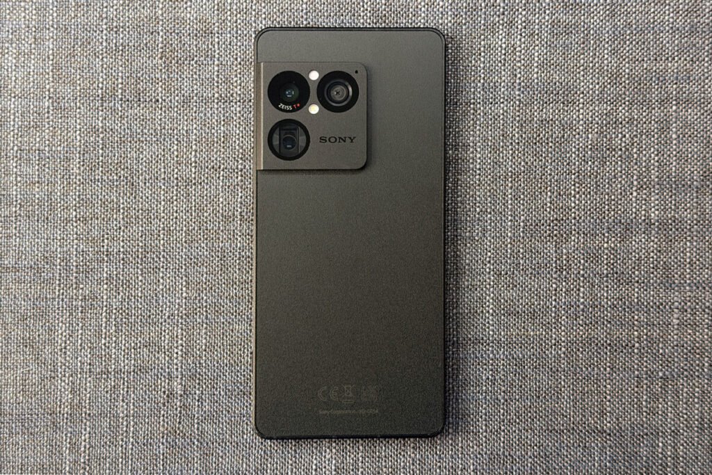 Vista frontal de la pantalla OLED encendida de el Sony Xperia 1 VIII junto a unos auriculares de cable conectados a su puerto superior de 3,5 mm.