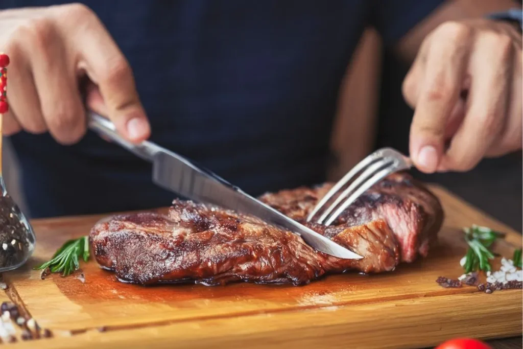 Corte de carne roja fresca sobre tabla de madera con verduras de acompañamiento, ilustración sobre consumo y riesgo de cáncer de colon