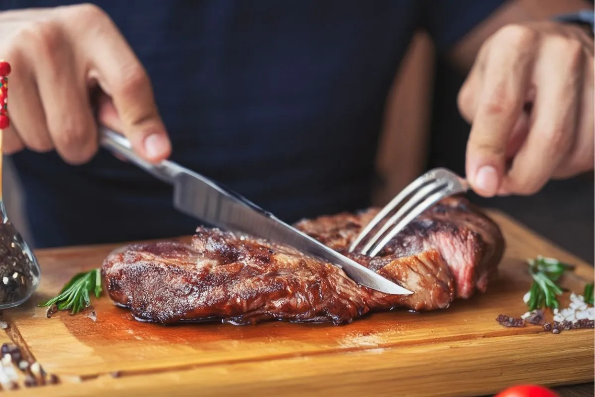 Corte de carne roja fresca sobre tabla de madera con verduras de acompañamiento, ilustración sobre consumo y riesgo de cáncer de colon