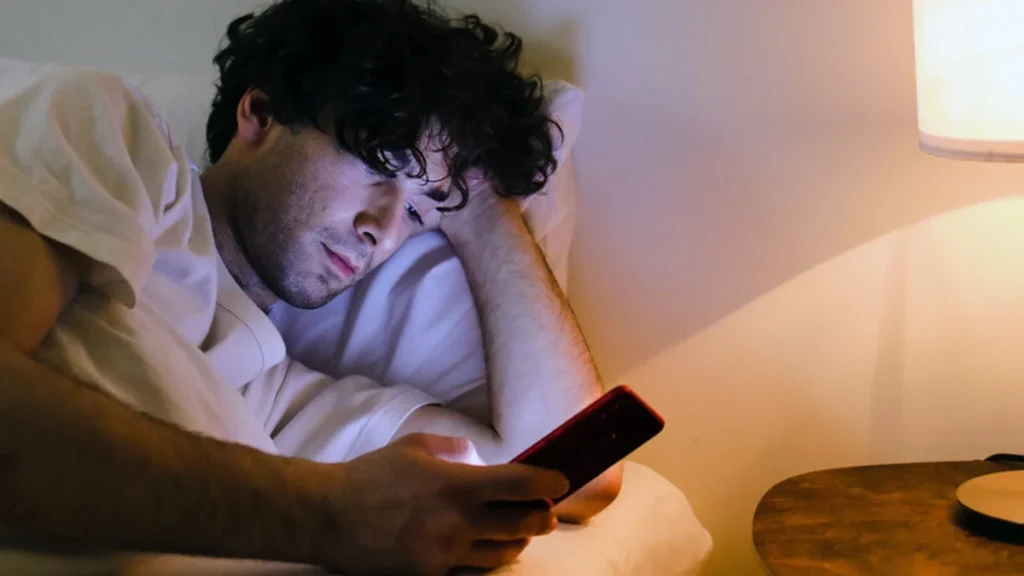 Smartphone descansando en la mesita de noche junto a una lámpara en modo nocturno